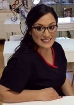 A woman wearing glasses is sitting at a table and smiling.