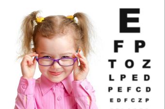 A little girl is wearing glasses in front of an eye test chart.