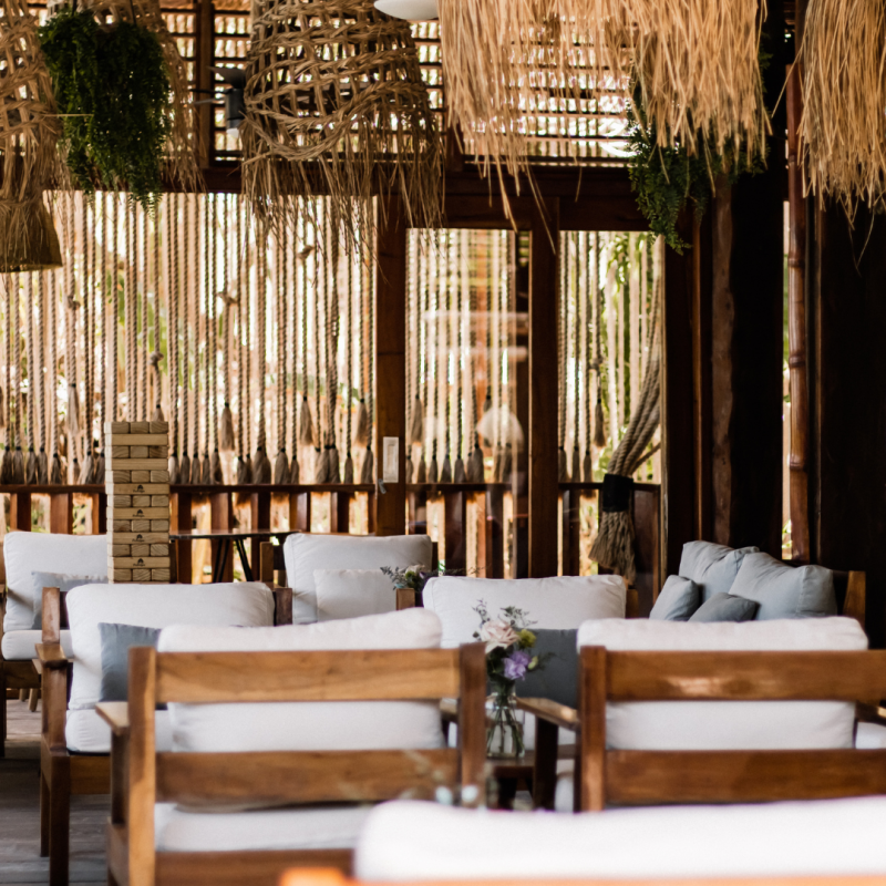 Wooden chairs with white cushions in a tropical-style room, bamboo walls, and woven light fixtures.