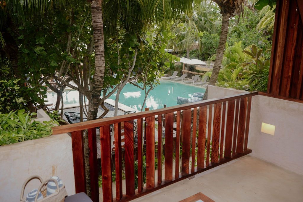 Balcony overlooking a turquoise pool surrounded by trees. Brown wooden railing.