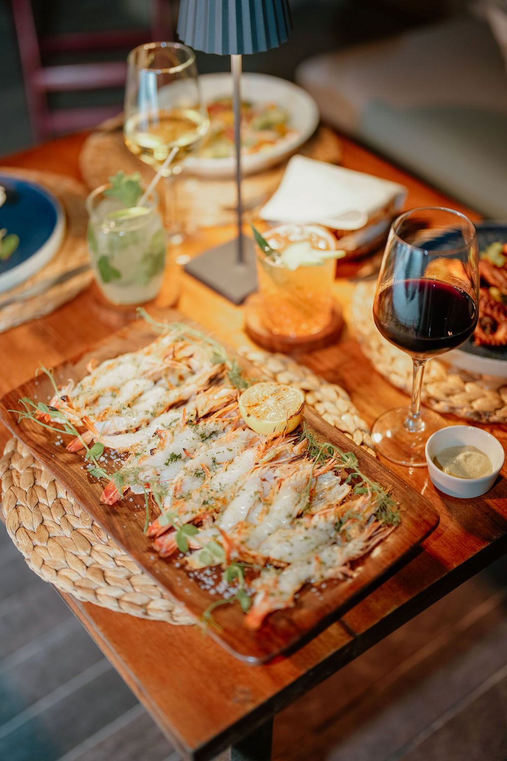 Wooden table with food and drinks: shrimp dish, wine glasses, cocktail, overhead shot.