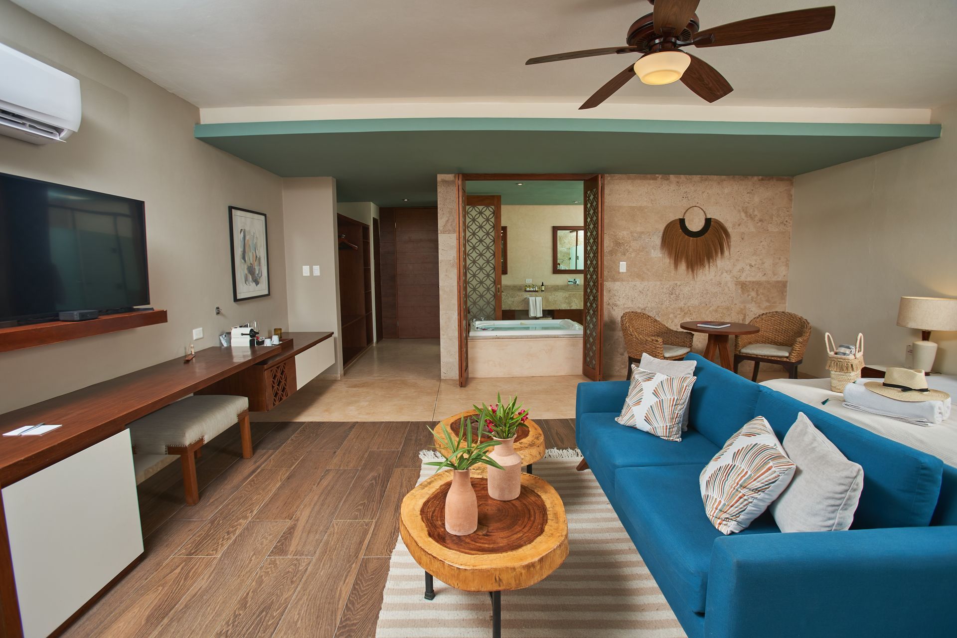 Luxury hotel room with teal sofa, wooden coffee tables, and view to a bathroom with a jacuzzi.