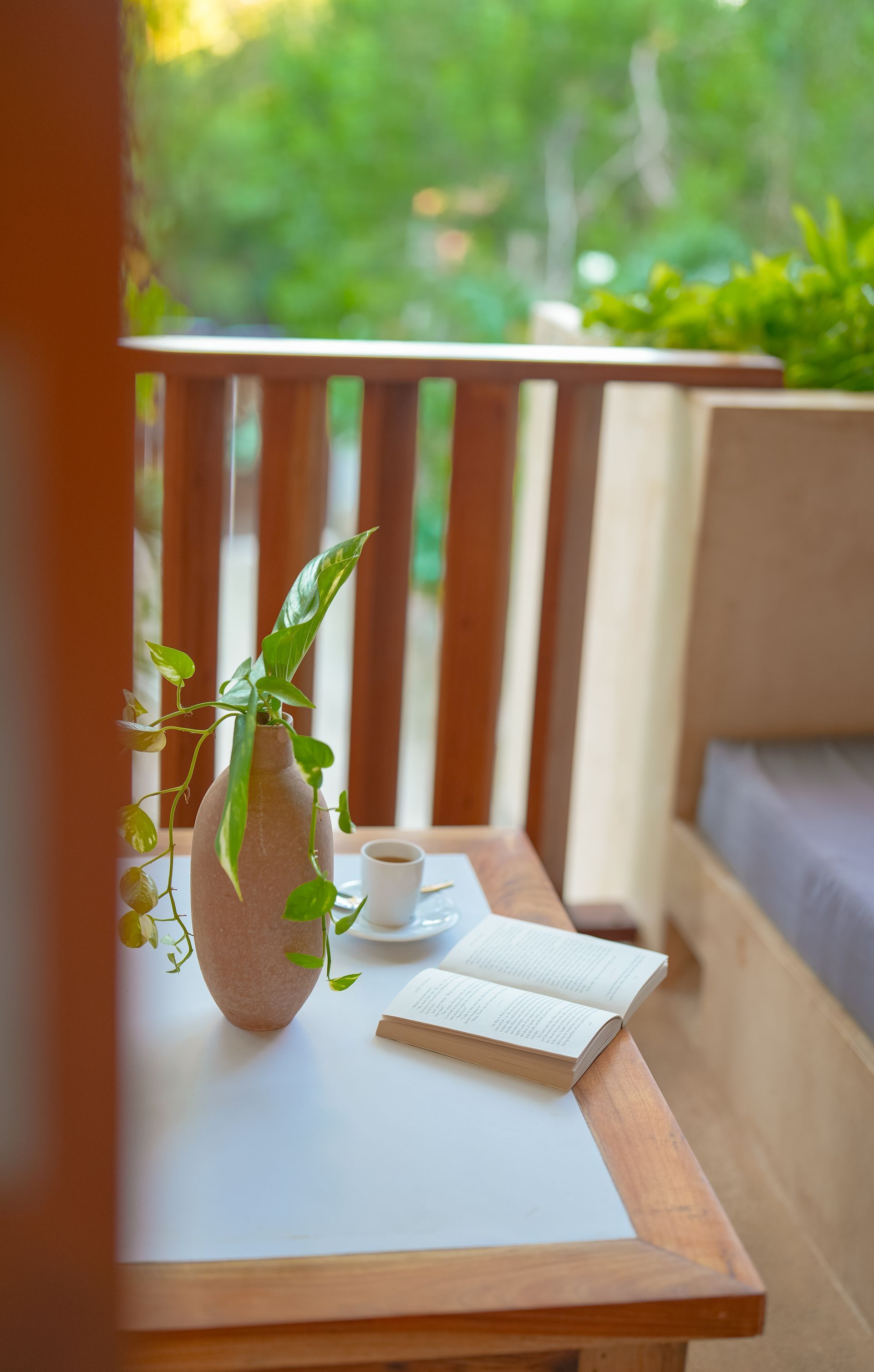 Wooden table on a balcony with a book, vase with greenery, and a cup of coffee.