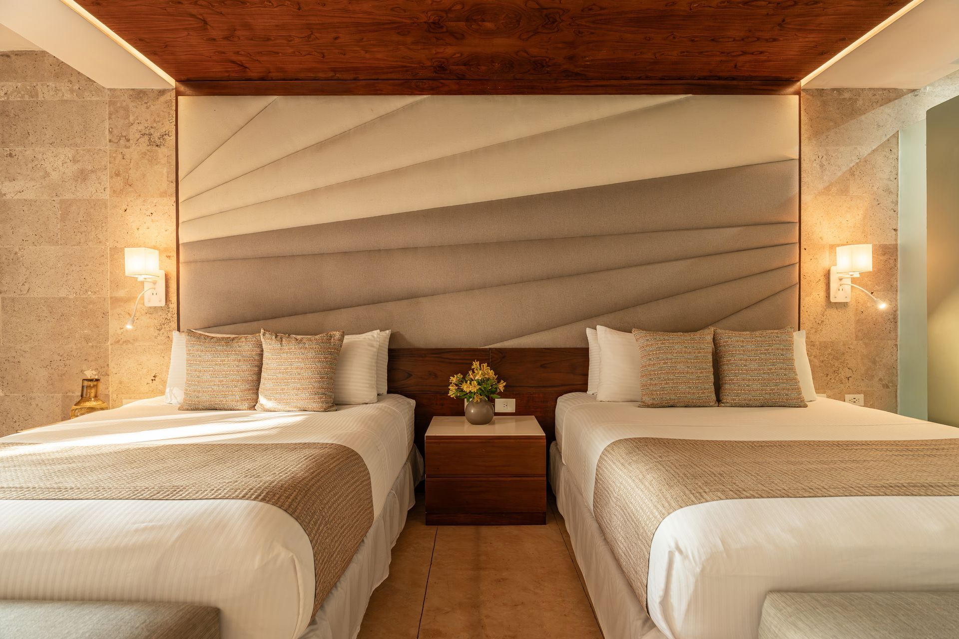 Hotel bedroom with two beds, decorative headboard, nightstand, and wall sconces.