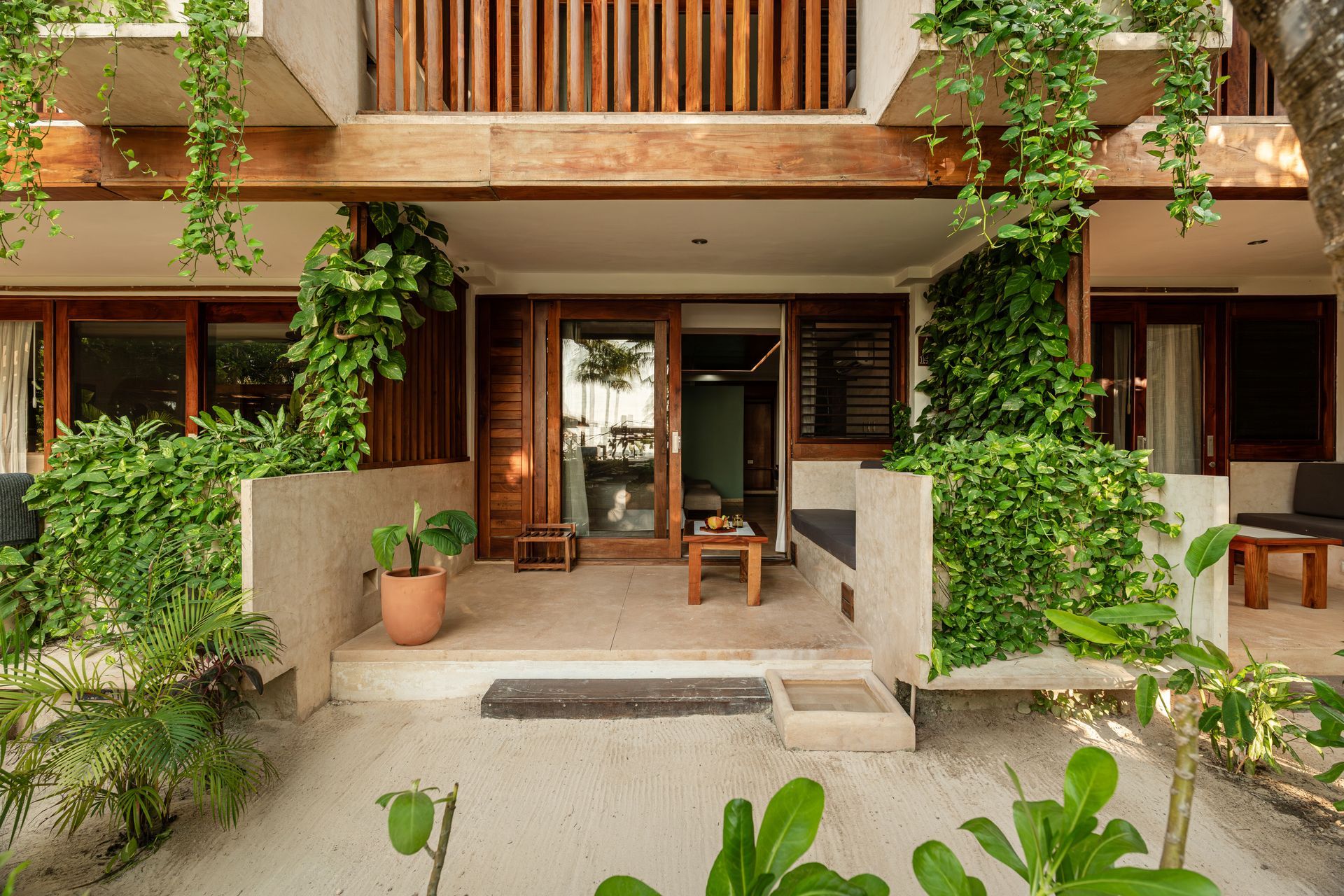 Exterior of a tropical hotel room with a wooden facade, porch, and climbing plants.
