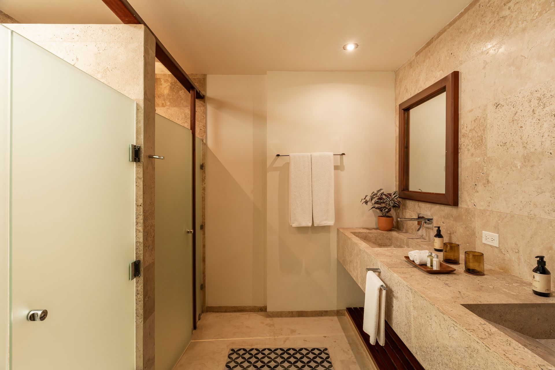 Bathroom with stone walls, a frosted glass shower, a double sink, and a wooden-framed mirror.