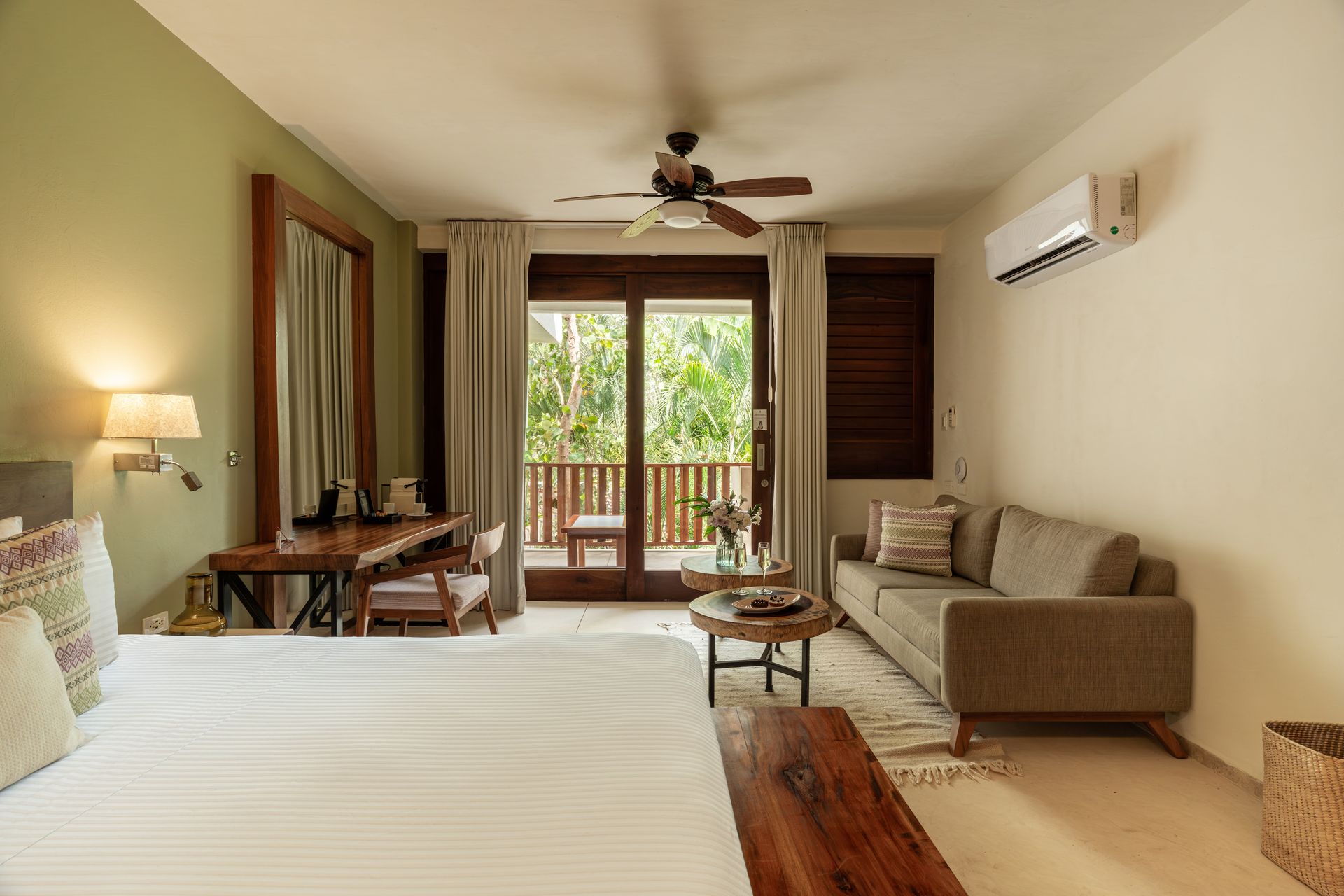 Bedroom with bed, desk, sofa, and balcony doors opening to a green outdoor view.