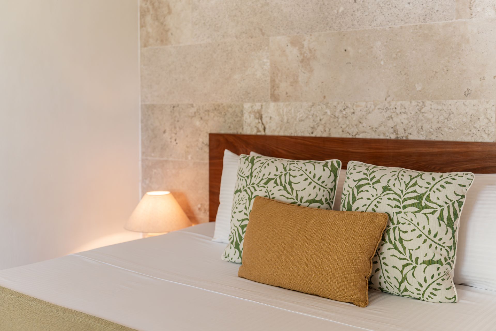 Bedroom with a bed, pillows, wooden headboard, and stone wall backdrop.