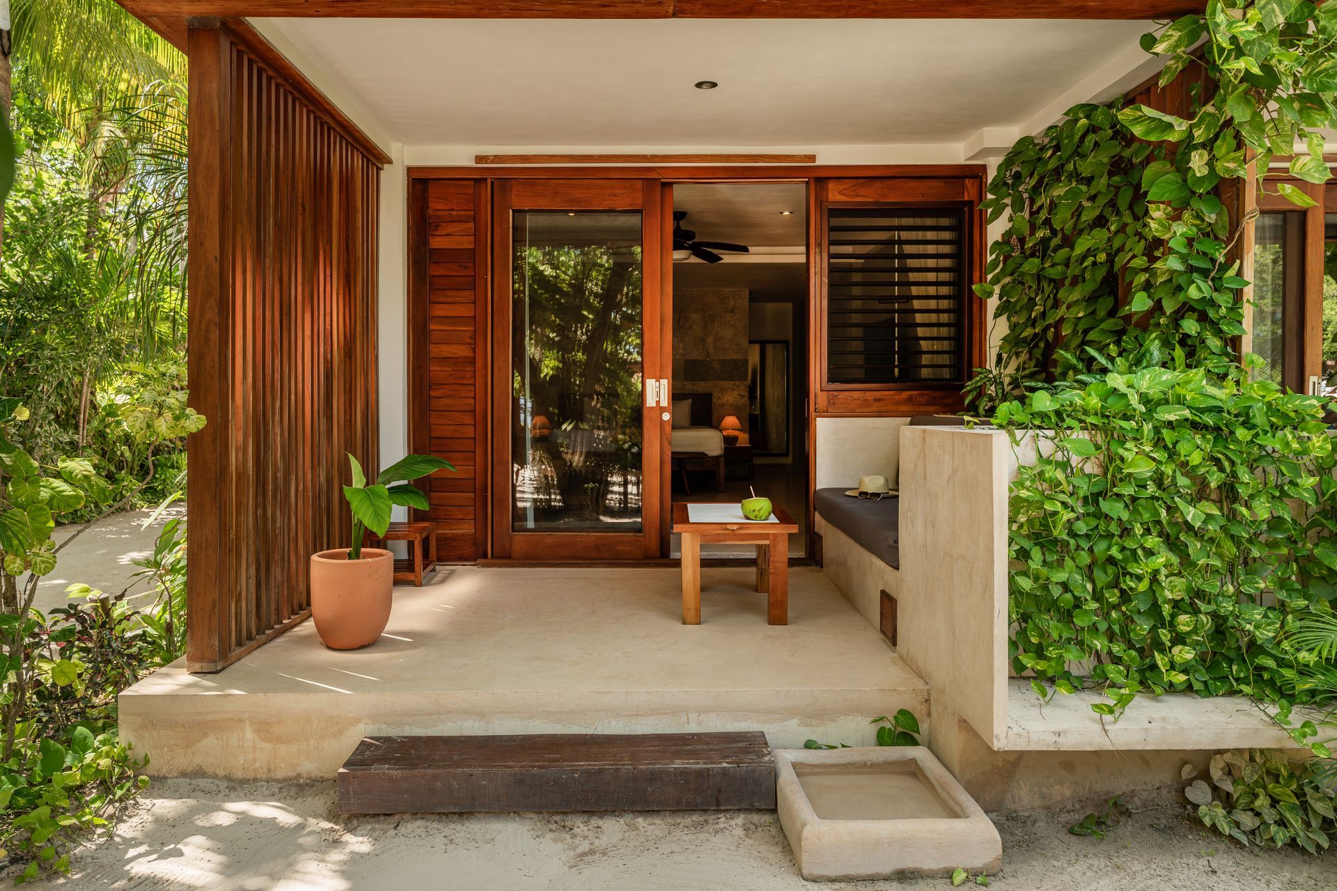 Wooden-framed outdoor patio with sliding glass doors, bench, and lush greenery.