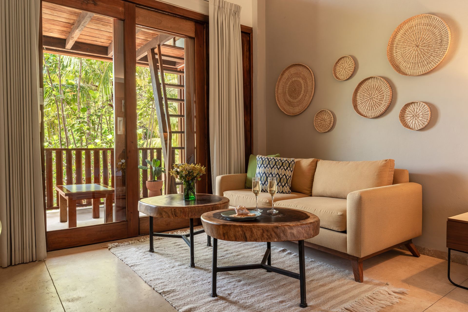 Living room with a beige couch, wooden tables, and a balcony overlooking trees. Wall decor.