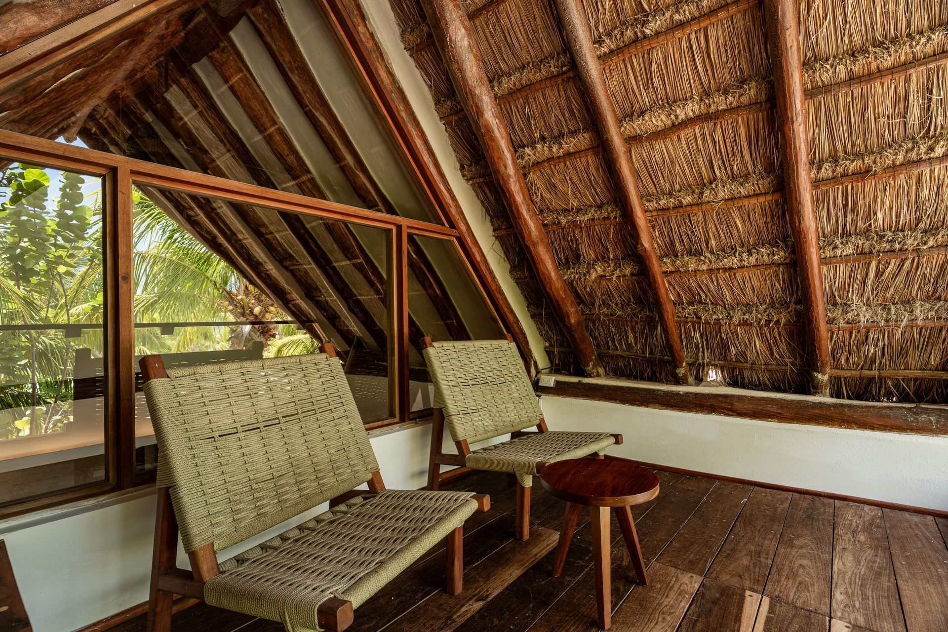 Two woven chairs and small table on a wooden balcony under a thatched roof.