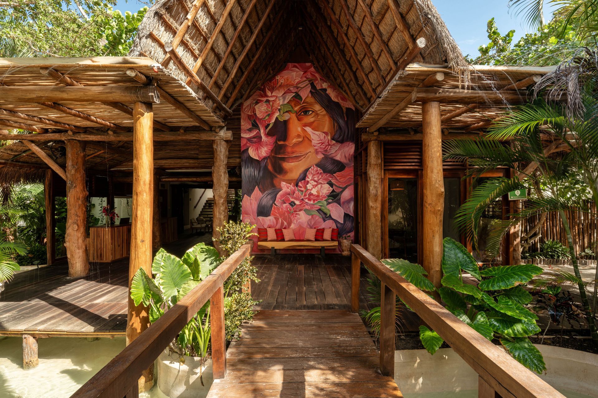 Wooden structure entrance with portrait framed in pink flowers; tropical setting.