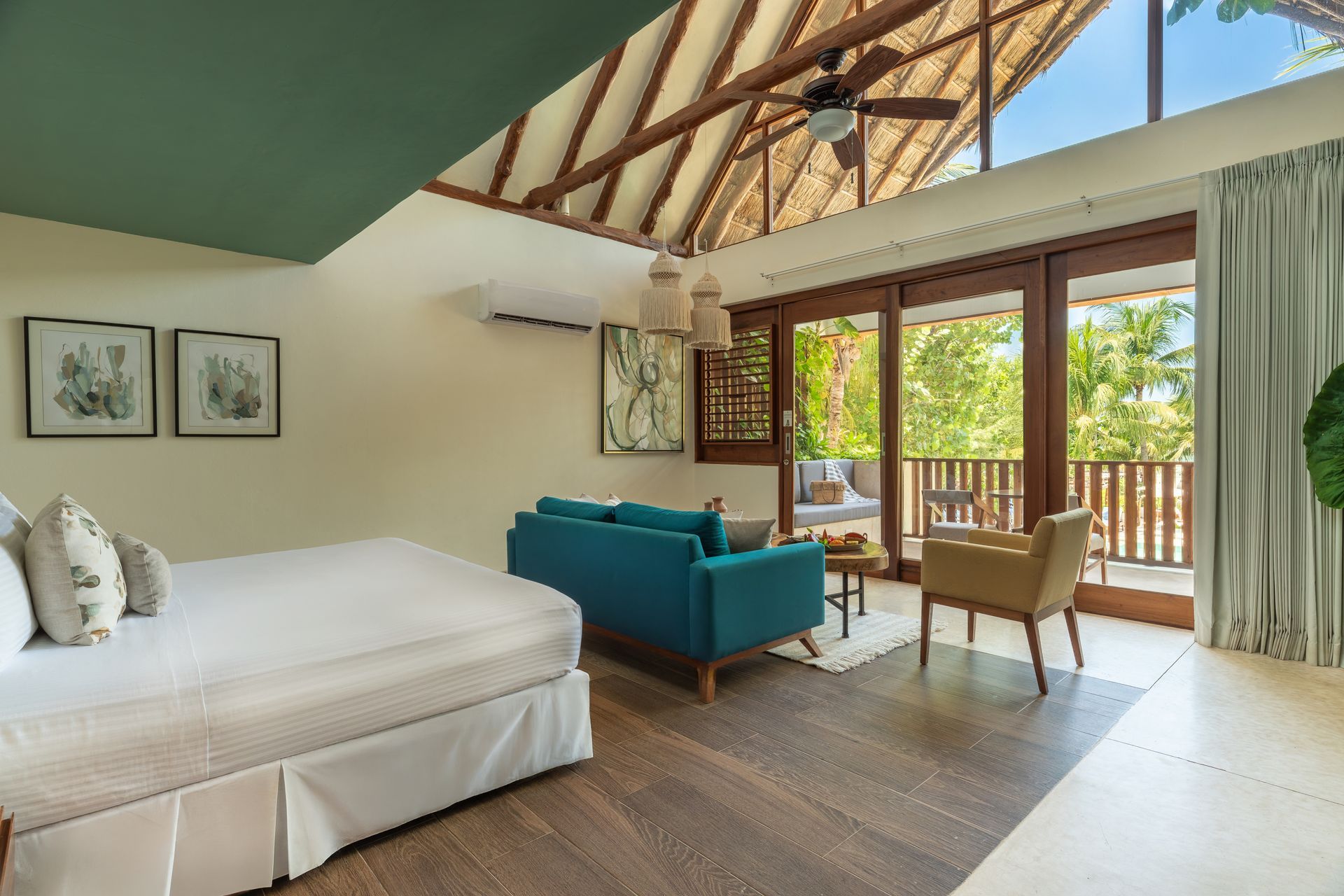 Bedroom with a bed, blue sofa, balcony, and high ceiling with natural light.