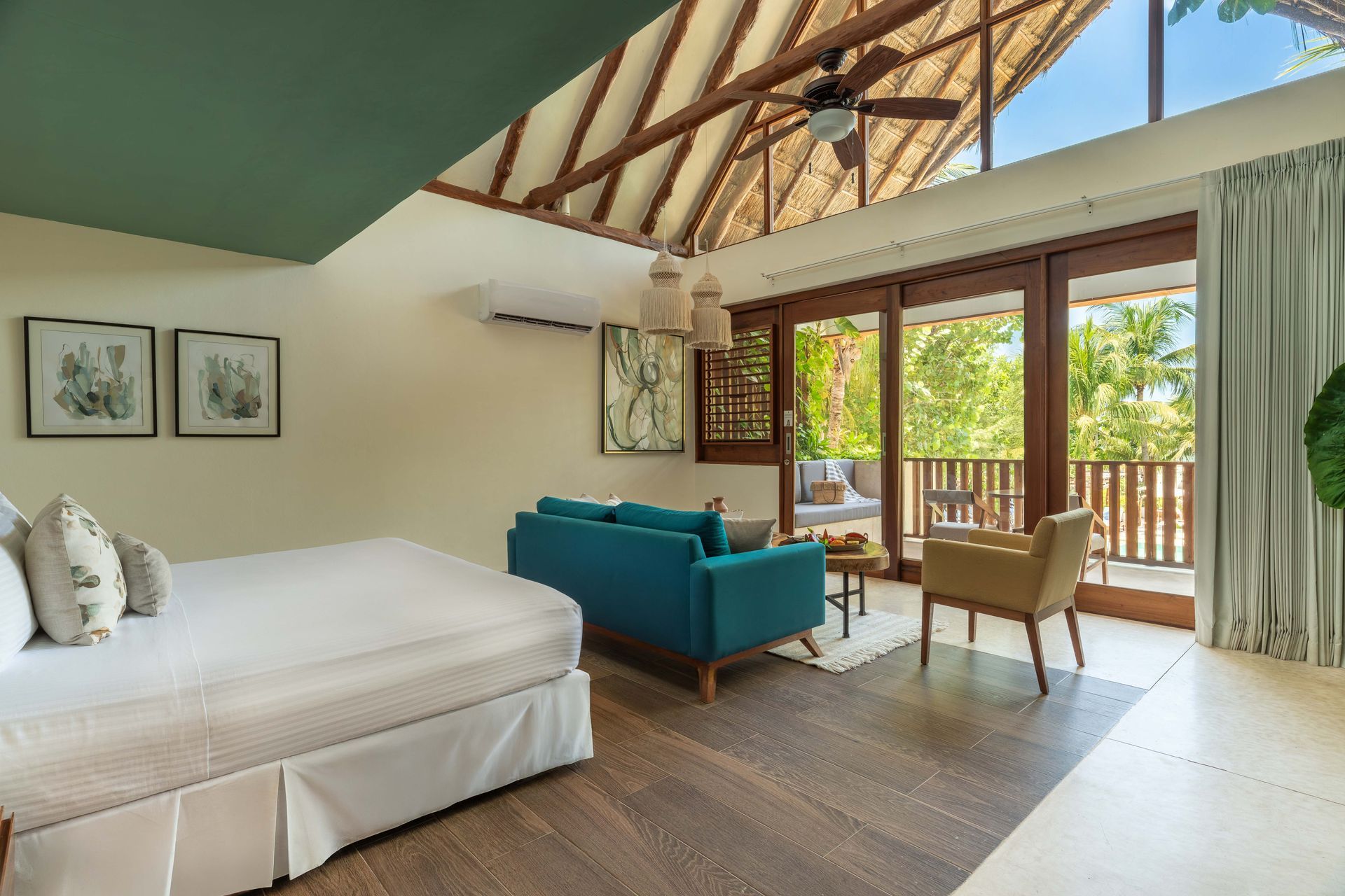 Bedroom with blue sofa, bed, and balcony overlooking tropical foliage.