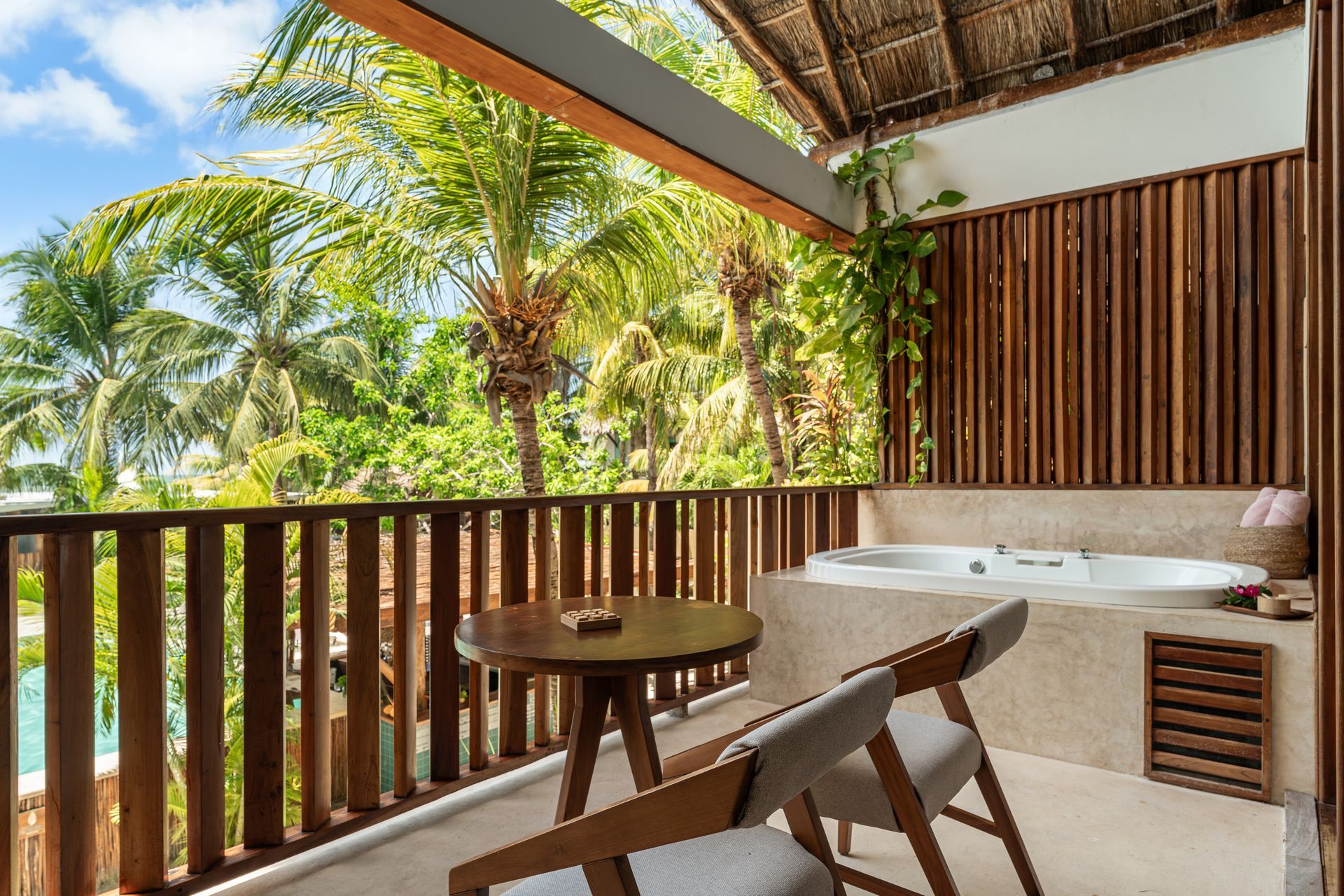 Balcony with jacuzzi, table, and chairs. Lush tropical foliage in background.