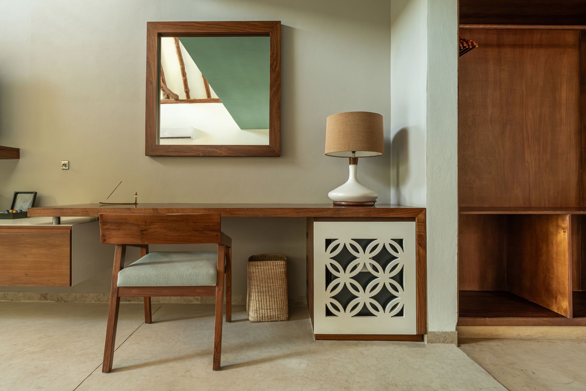 Desk with chair, lamp, mirror, and built-in closet in a room with neutral walls.