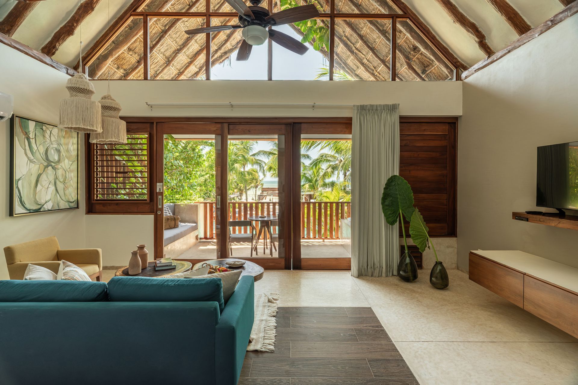 Living room with teal sofa, wooden balcony, and high, thatched ceiling.