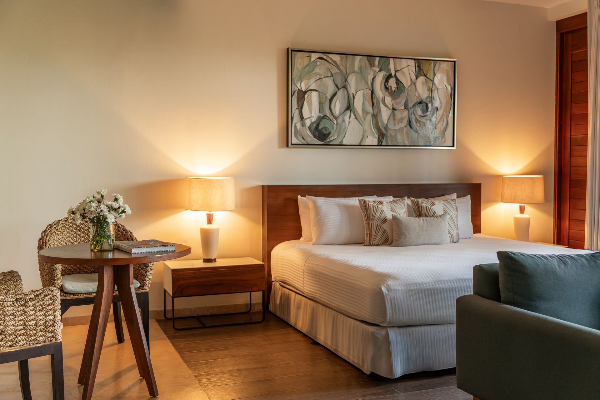 Cozy hotel room with a bed, small round table, armchair, and lamps.
