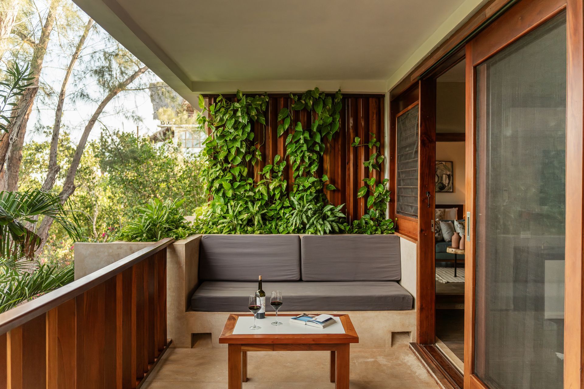 Balcony with sofa, living wall, wooden table with wine glasses, and open sliding door to interior.