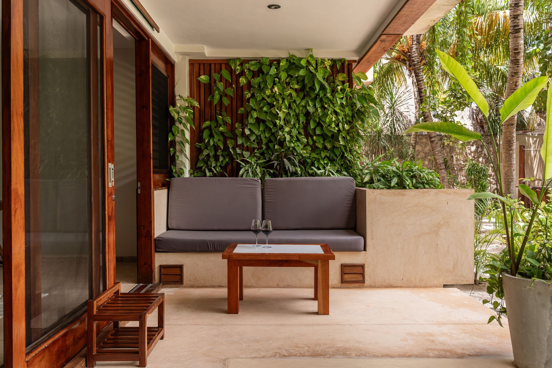 Patio seating with gray cushions, a wooden table, and lush greenery.