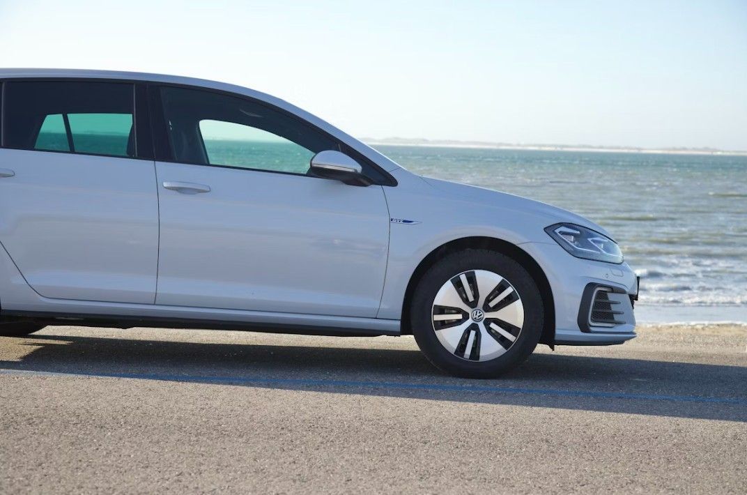 White electric car parked near a beach with ocean in the background.