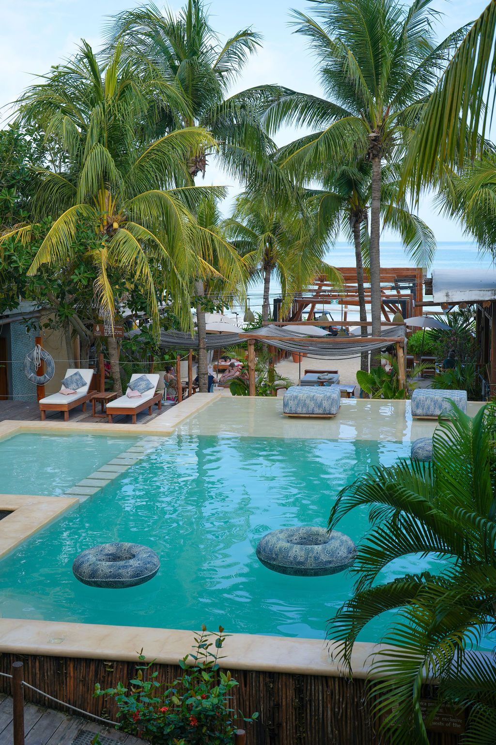 Pool surrounded by palm trees and lounge chairs at a tropical resort.