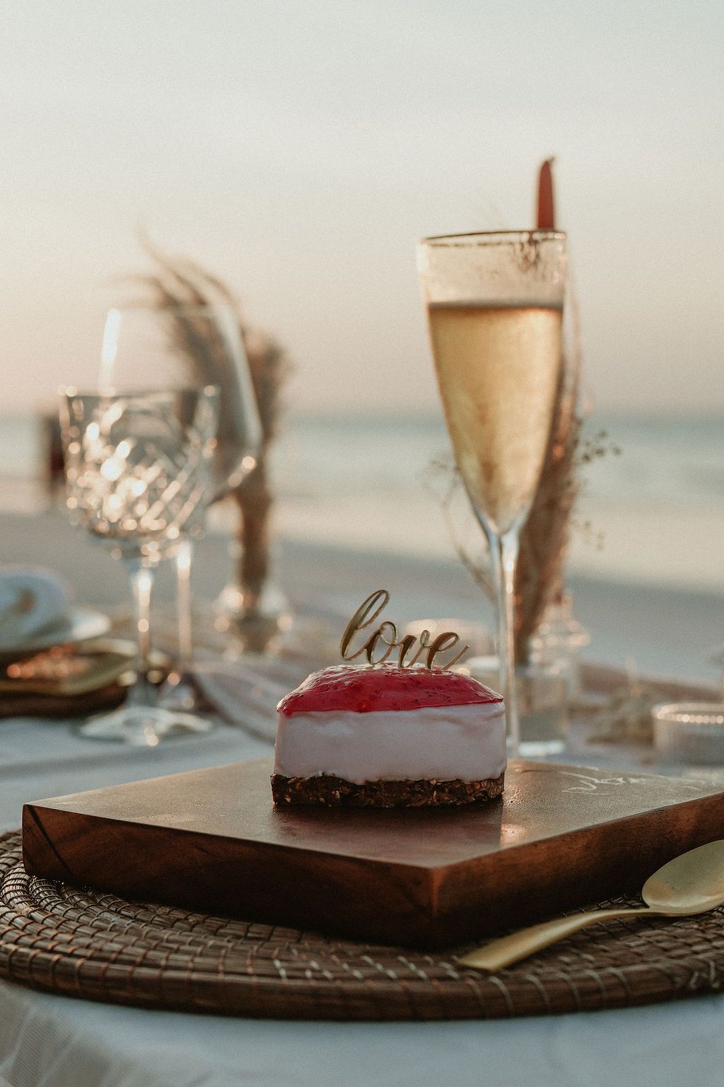 Romantic beach table setting with cake, champagne, and ocean view.