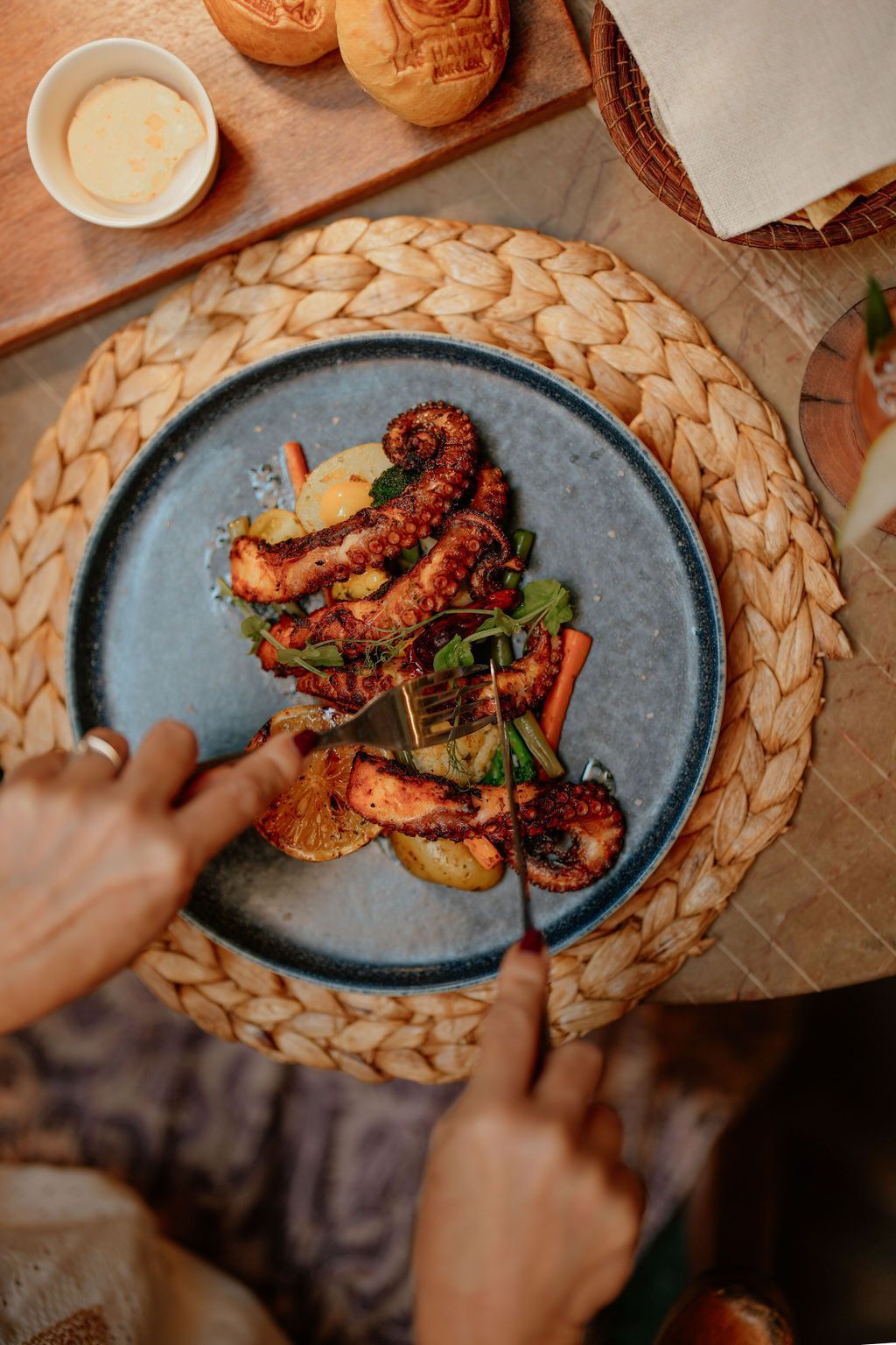 Overhead shot of grilled octopus dish being cut with a knife and fork on a blue plate.