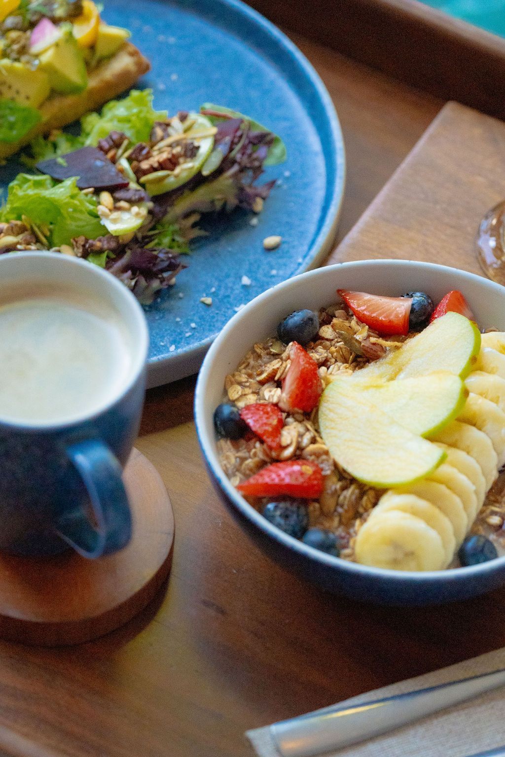 Breakfast on a tray: avocado toast, oatmeal with fruit, and coffee.