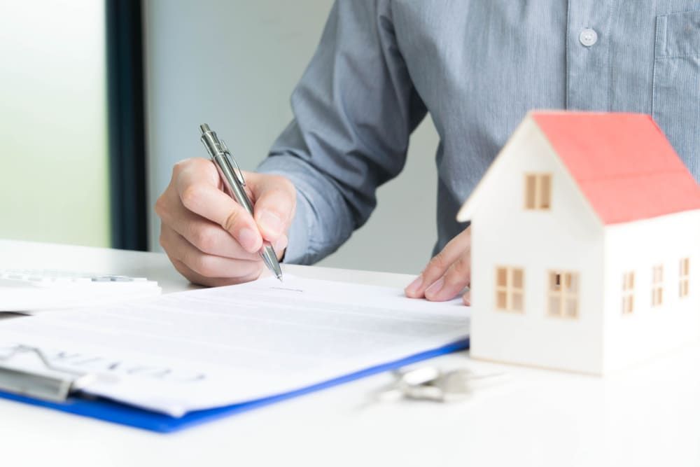 A Man is Signing a Document Next to a Model House — North Coast Conveyancing In Laurieton, NSW