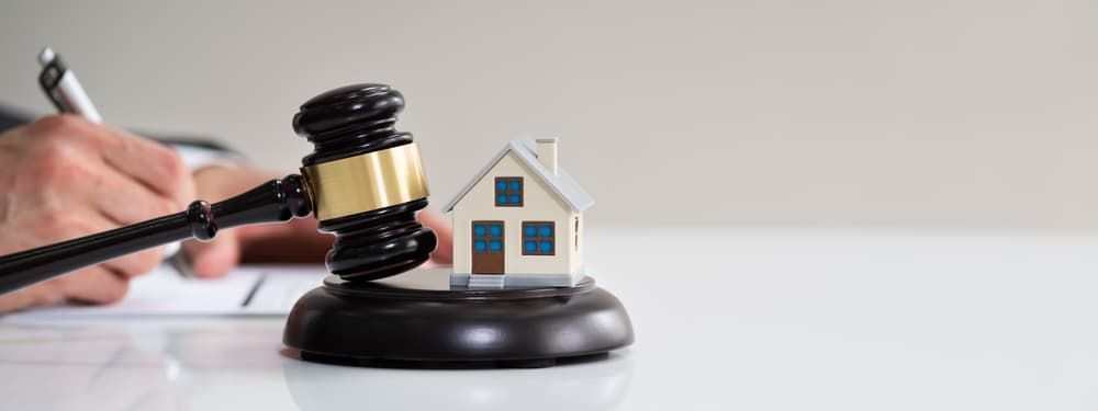 A Person is Holding a Gavel Next to a Model of a House — North Coast Conveyancing In Port Macquarie, NSW