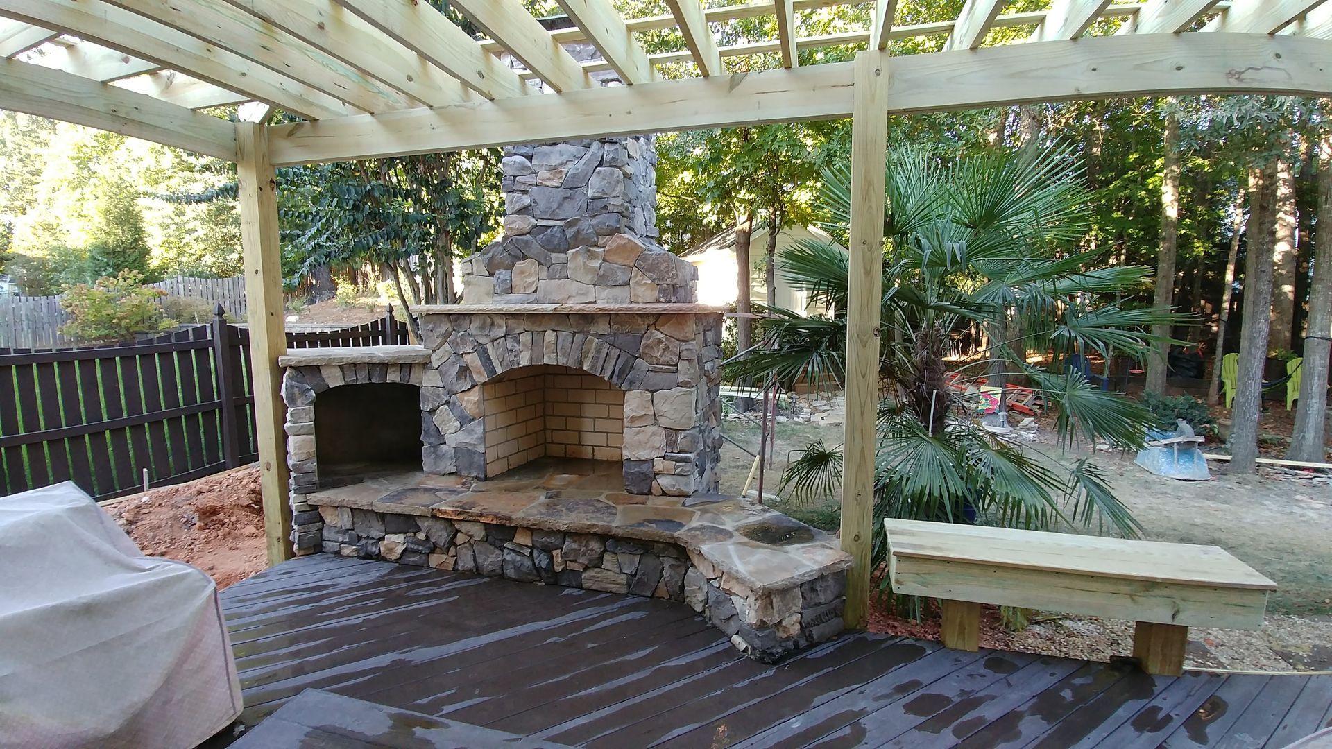 Stone fireplace with a wooden pergola in an outdoor setting.