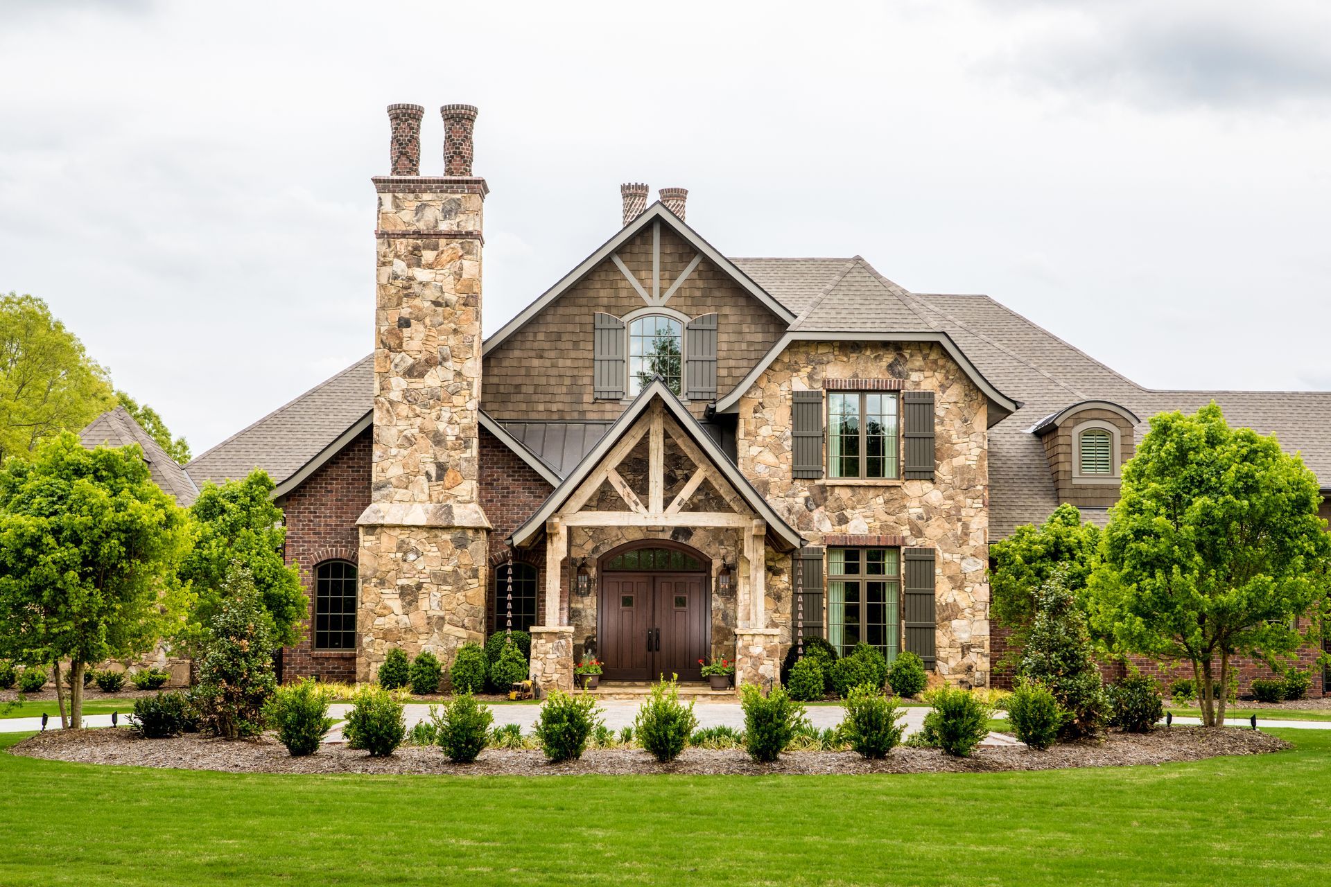 Stone and brick luxury home with a large chimney and green shutters.