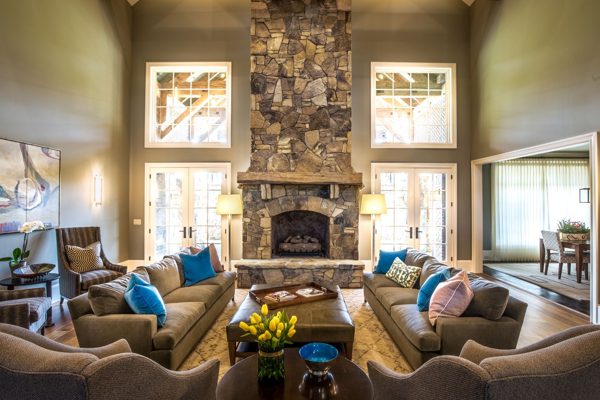 Living room with a stone fireplace, two sofas with blue and pink pillows, and large windows.