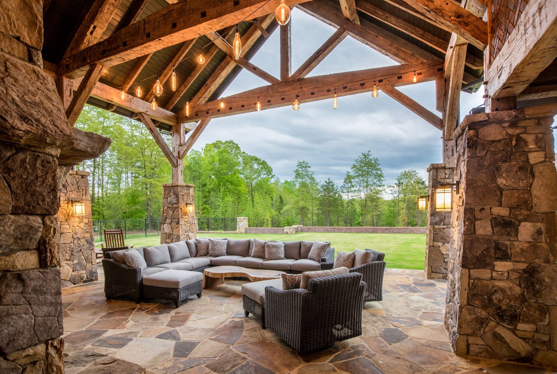 Stone patio with sectional seating, a wood beam ceiling, and a view of a grassy lawn and trees.