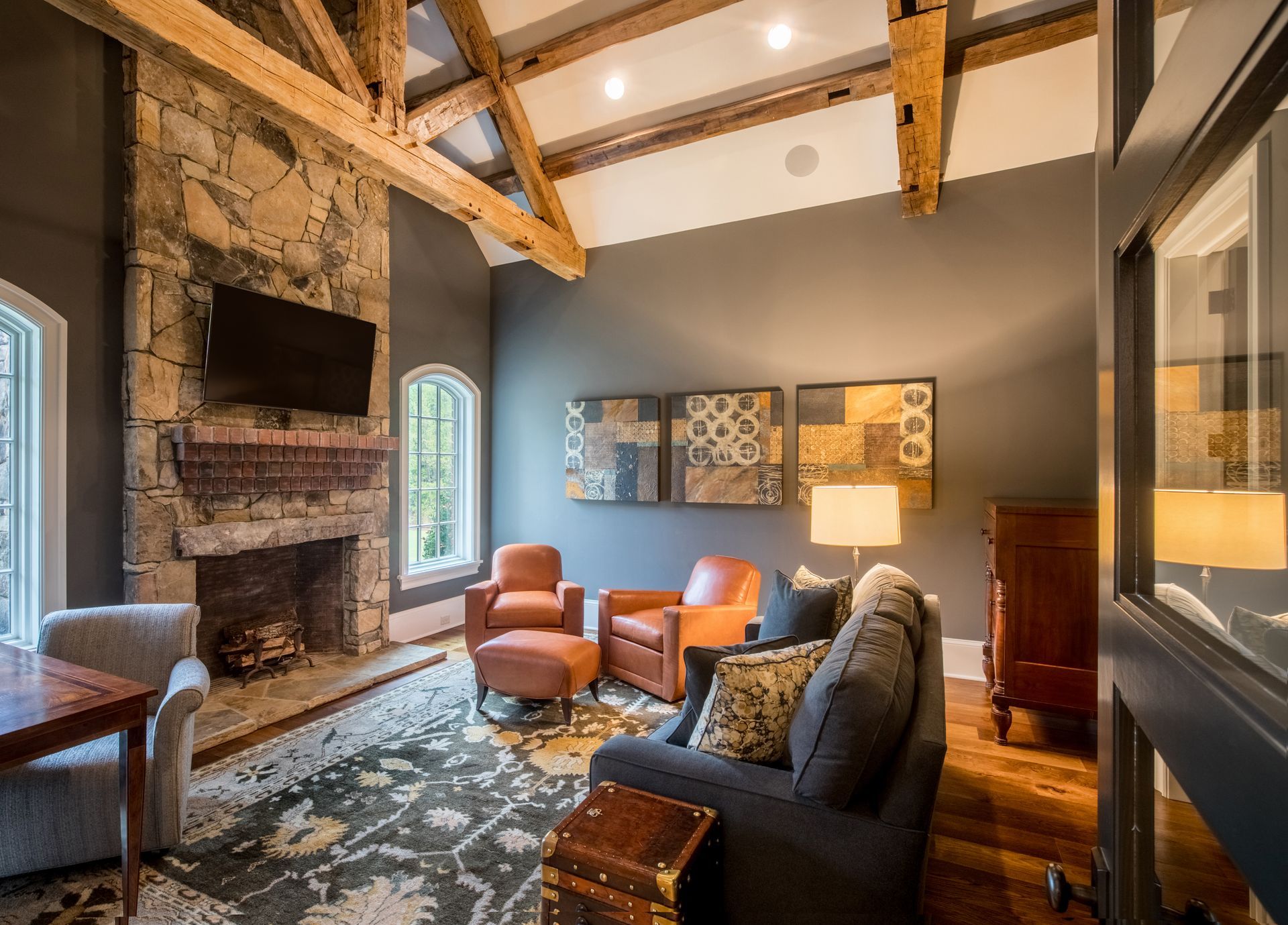 Living room with stone fireplace, wooden beams, dark gray walls, and leather furniture.