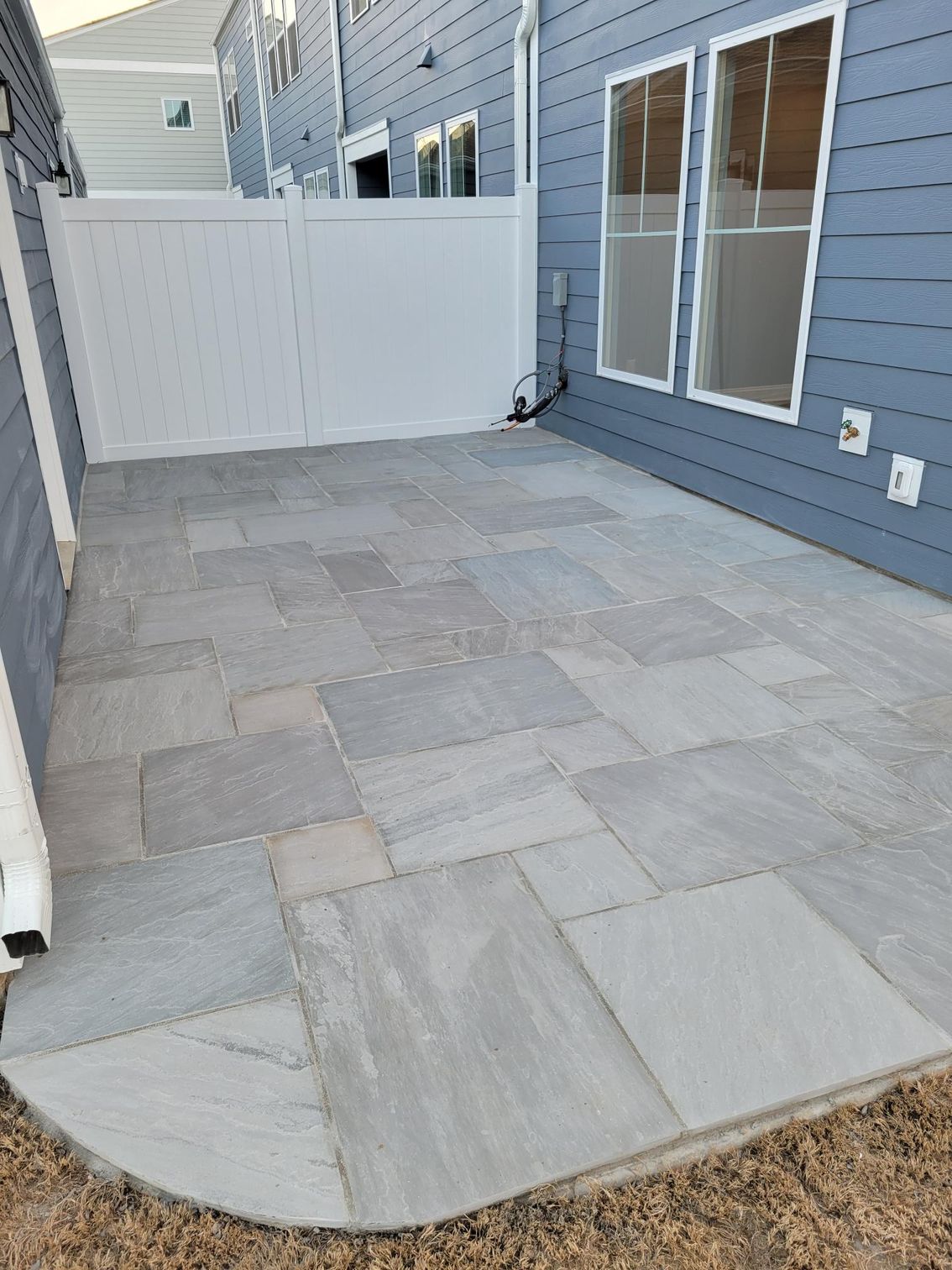 Patio with gray pavers, white fence, and blue siding.