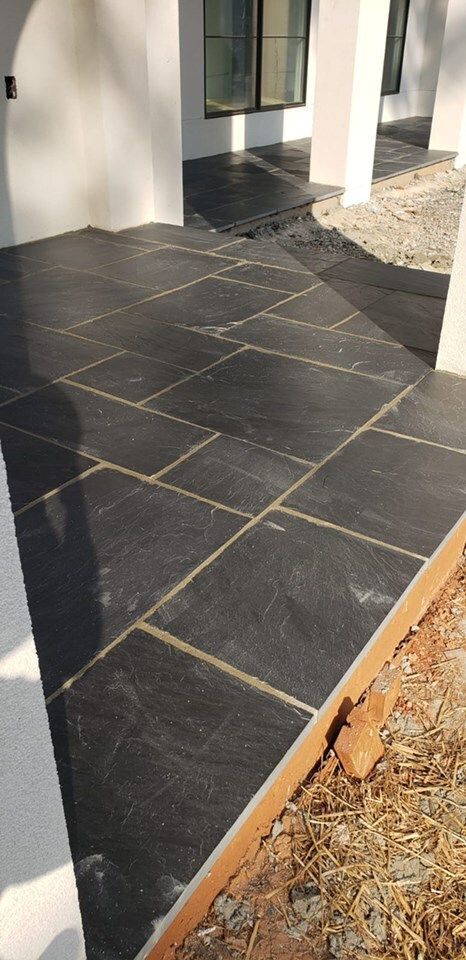 Black tiled patio with white columns and wall; gravel and dirt border.