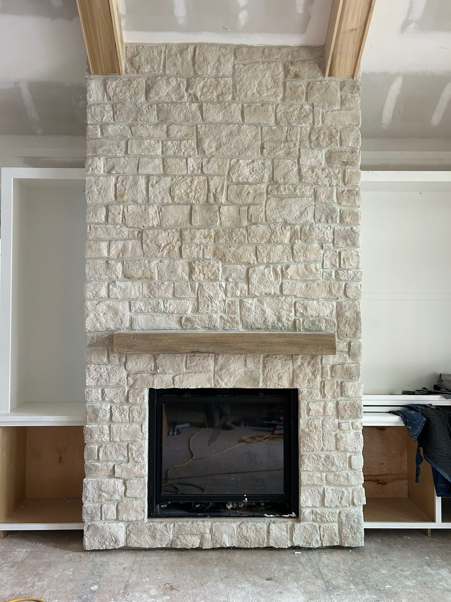 Stone fireplace with wooden mantel and built-in white cabinets.