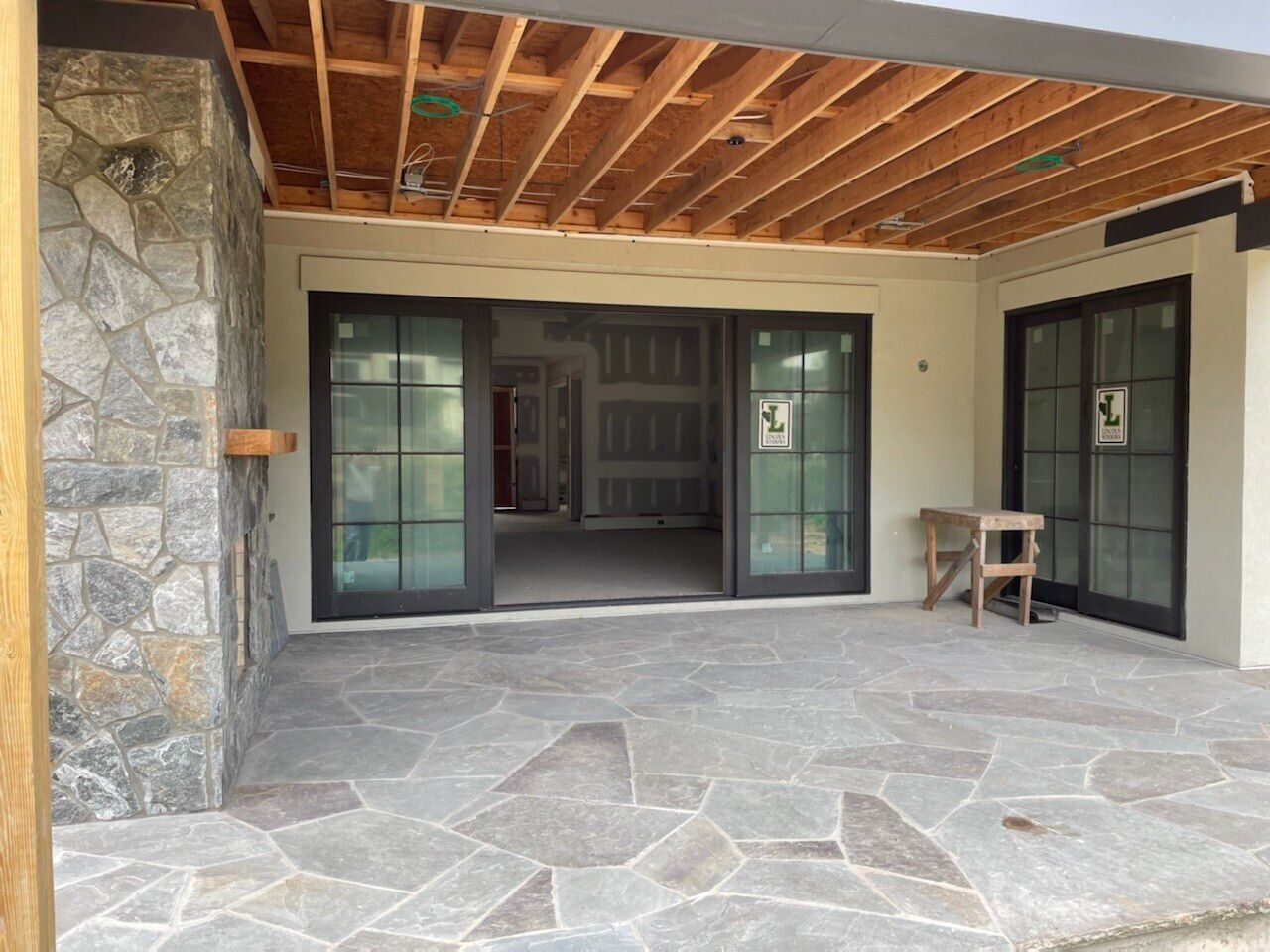 Stone patio with dark framed sliding glass doors, exposed wood ceiling, and stone wall.