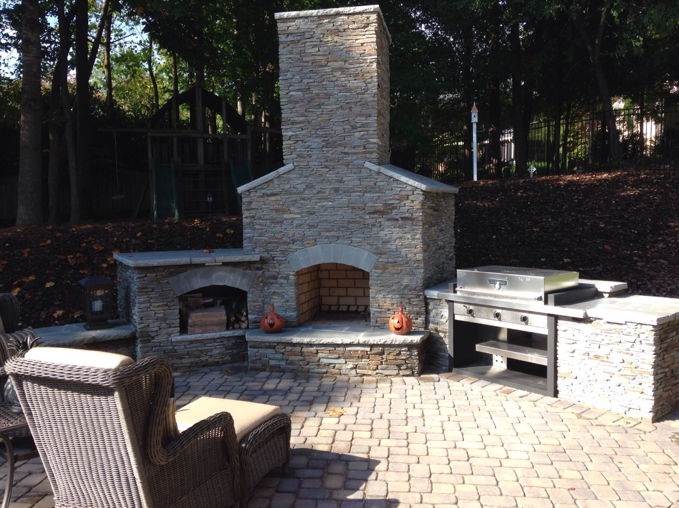 Stone outdoor fireplace with grill, wood storage, and patio.