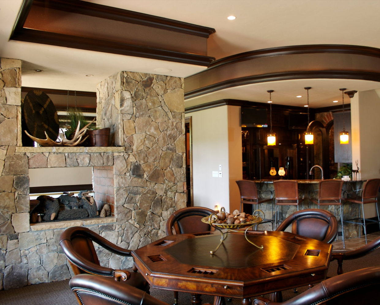 Game room with stone fireplace, bar, and poker table. Leather chairs and dark wood accents.