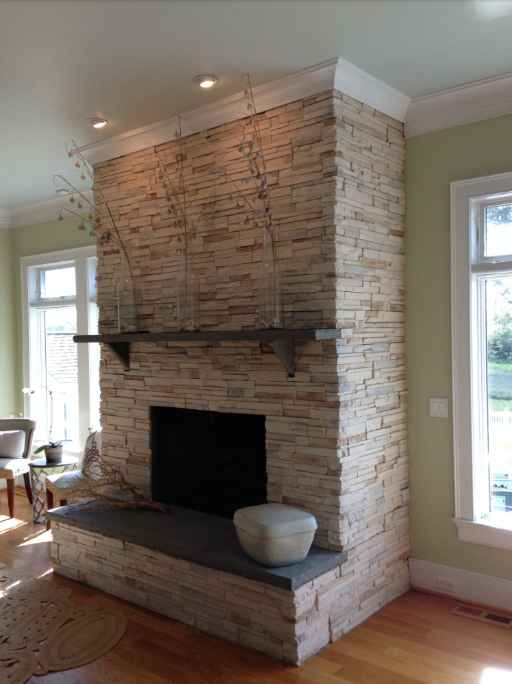 Stone fireplace with a dark mantel and hearth in a living room with light green walls.