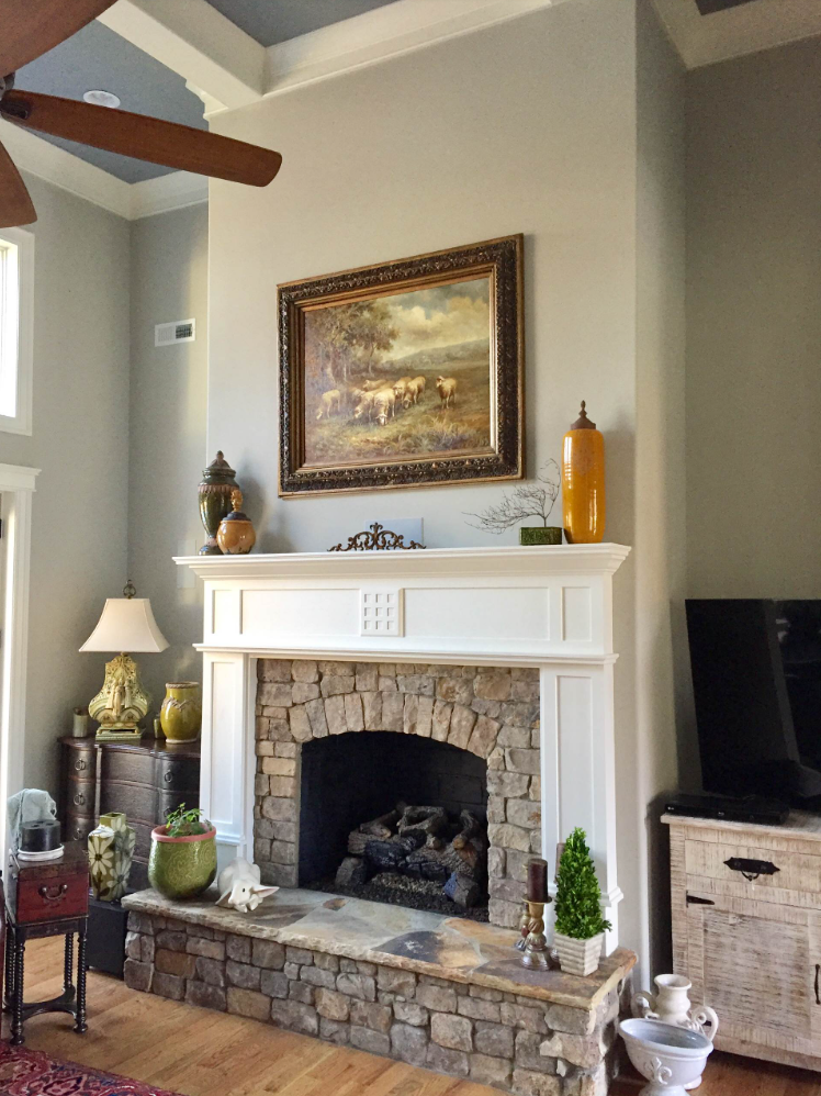Fireplace with stone facade, arched opening, and white mantelpiece, framed painting above, and decor.