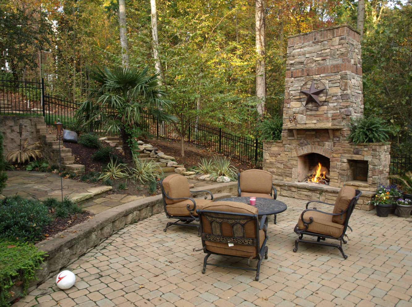Outdoor patio with fireplace, seating, and lush greenery.