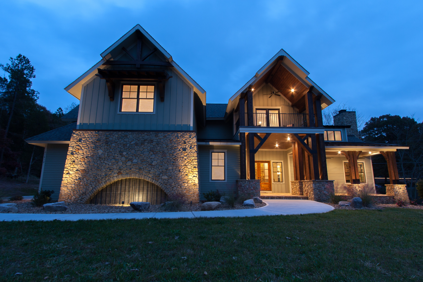 Large, two-story house with stone and wood accents, illuminated at dusk against a blue sky.