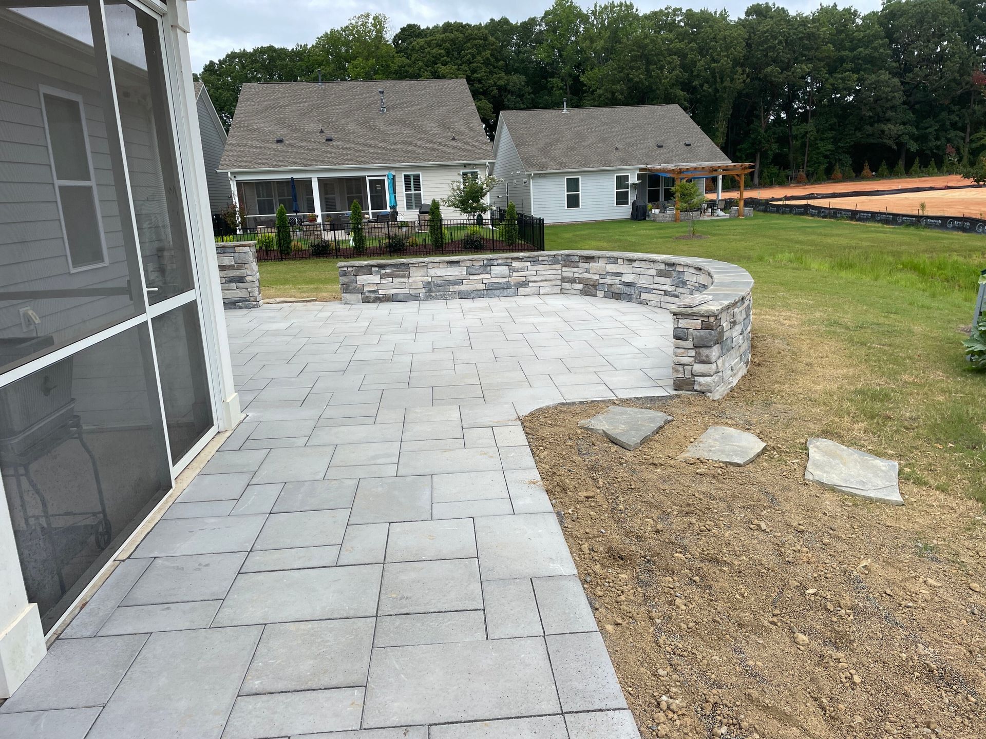 Stone patio with curved wall, next to a grassy area, and houses in the background.
