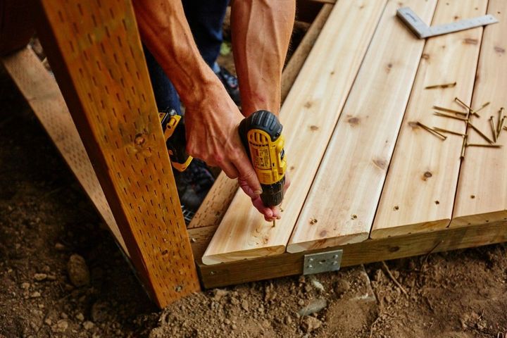 Person using a drill to fasten a wooden deck board outdoors