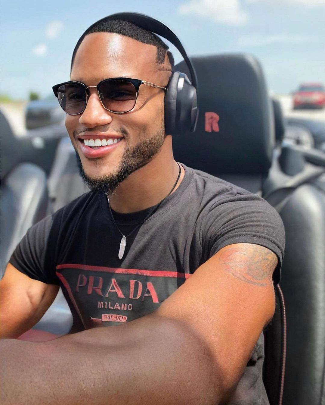 A man wearing headphones and sunglasses is wearing a prada shirt
