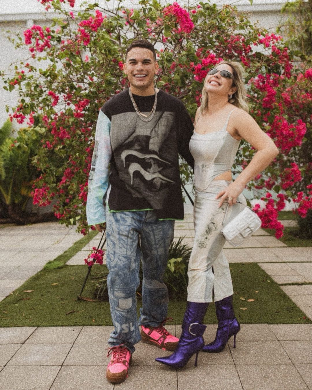 A man and a woman are standing next to each other in front of a bush with pink flowers.